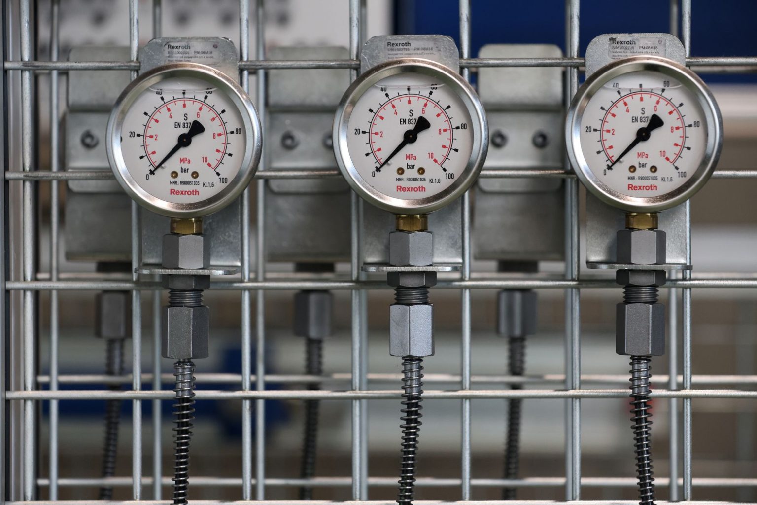 Close de manômetros industriais instalados em uma grade metálica dentro de uma fábrica.