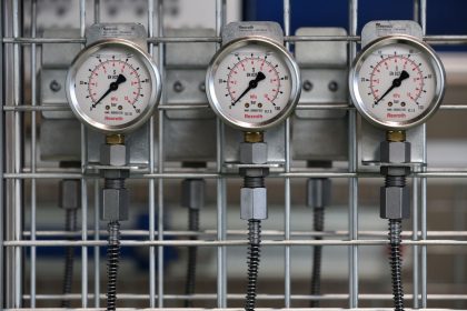 Close de manômetros industriais instalados em uma grade metálica dentro de uma fábrica.