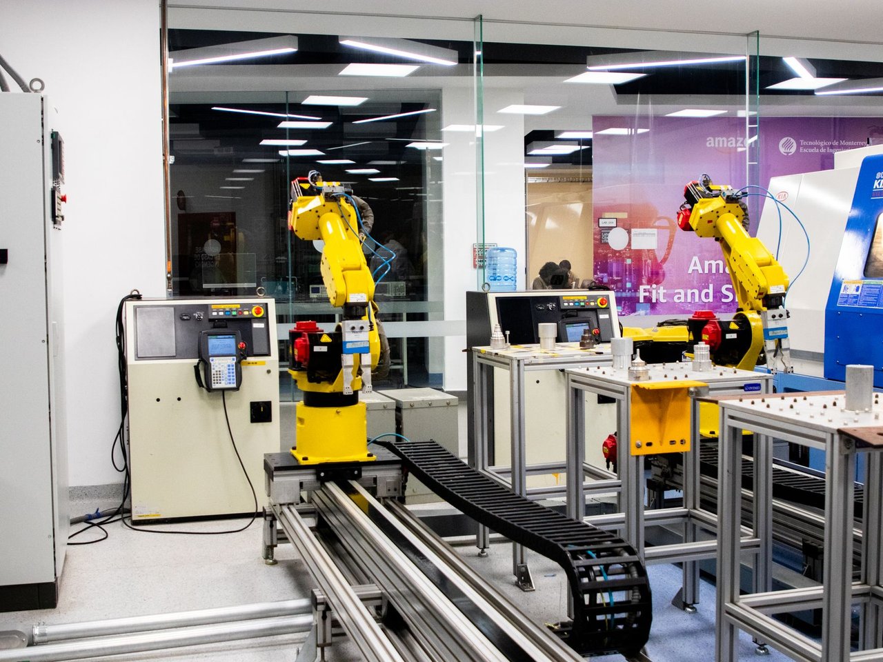 Braços robóticos operam em um ambiente industrial moderno, com equipamentos de controle ao fundo.