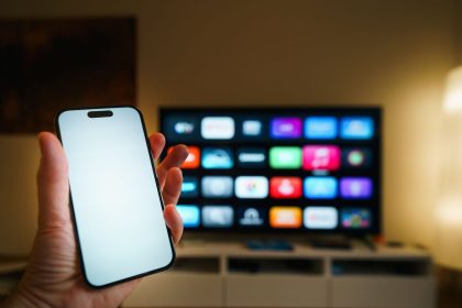 Smartphone em primeiro plano diante de uma televisão inteligente com aplicativos exibidos em uma sala de estar.