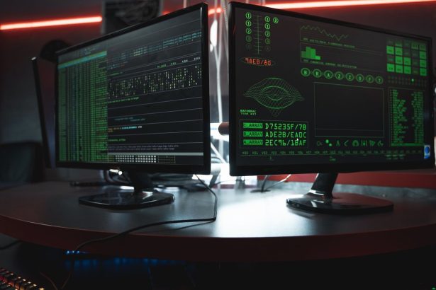Dois monitores exibem interfaces de código em uma sala escura, em referência à segurança digital.